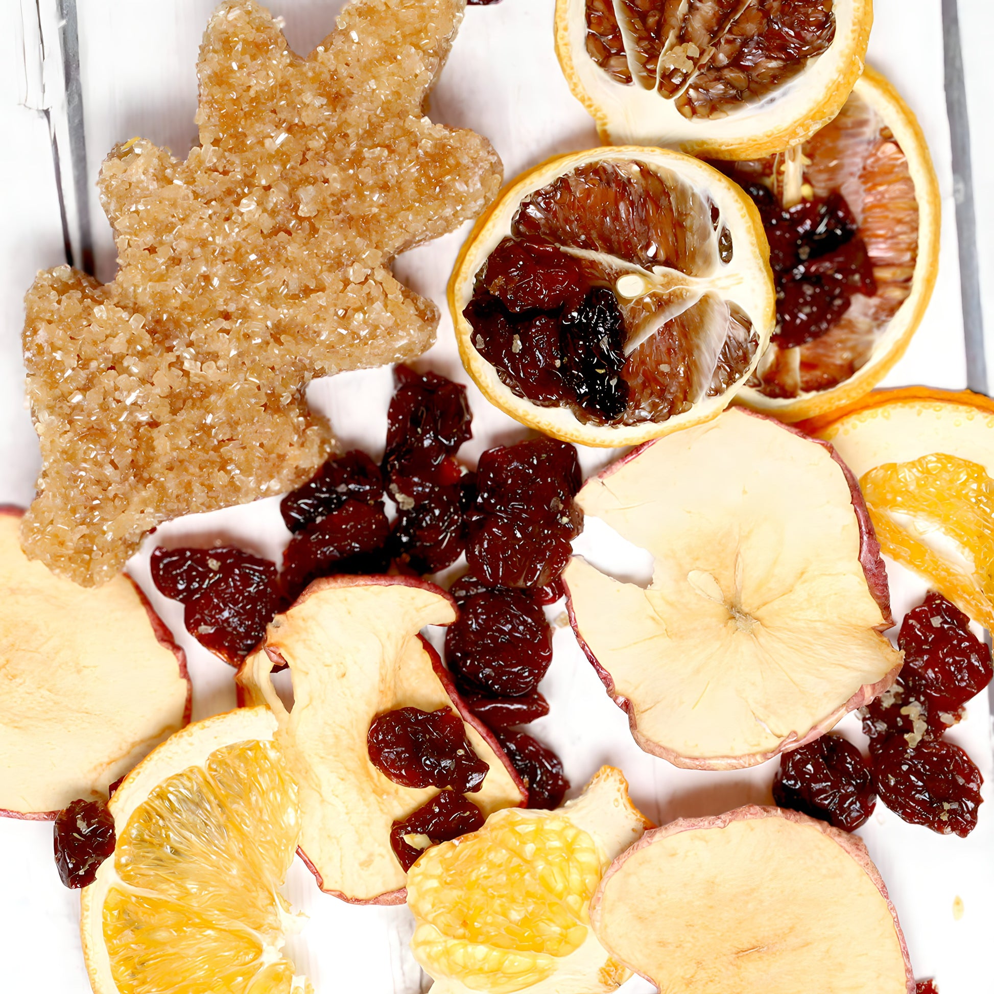 A variety of dried fruits including slices of lemon, apple, and orange are displayed alongside dried cranberries and a leaf-shaped cookie dusted with sugar on a light wooden surface. The composition highlights the diverse colors and textures of Oak & Sugar's Sunny Day Sangria Infusion Kit, making it perfect for crafting your ideal fruity blend.