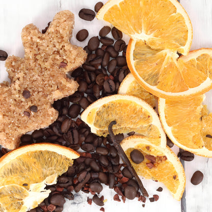 Slices of fresh orange, coffee beans, a sprig of vanilla, and a brown sugar treat shaped like a maple leaf are arranged on a white wooden surface. The various textures and colors create a vibrant and inviting composition reminiscent of Oak & Sugar's Holiday Spice Java Martini Cocktail Infusion Kit - LIMITED EDITION.